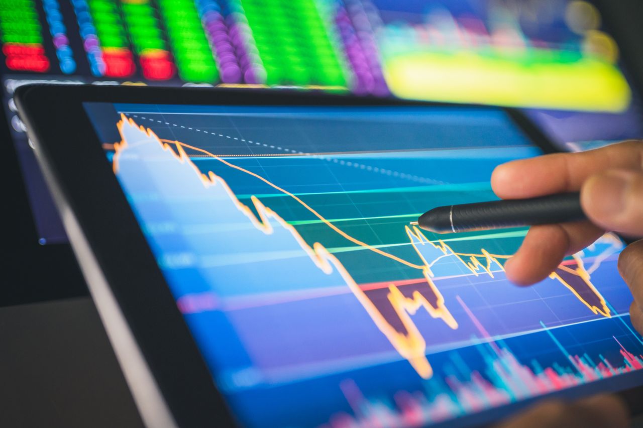 closeup of person looking at blue stock market chart and pointing at screen with a pen