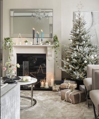 Living room with cream carpet, fireplace with mantelpiece, coving and picture rail in grey, pale grey and beige soft furnishings, decorated Christmas tree in the corner.