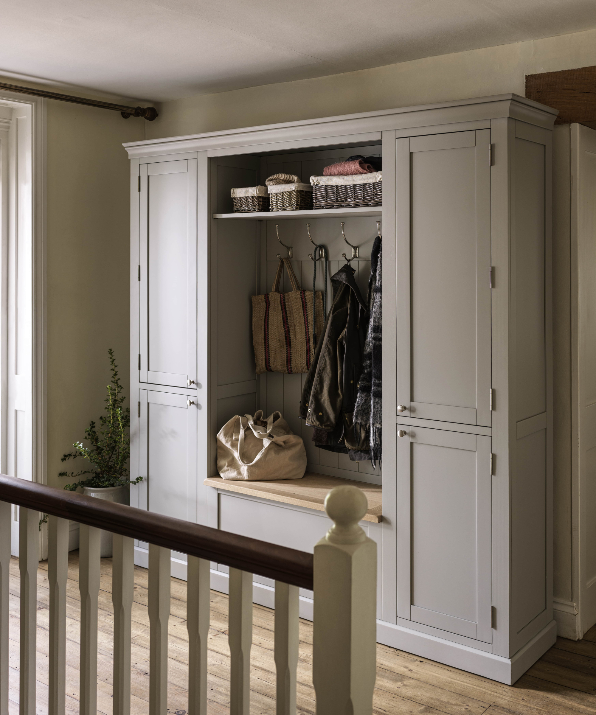 freestanding pale grey boot room unit with cupboards either side, shelf, seat in middle and hooks on back panel placed on landing area with wooden floor