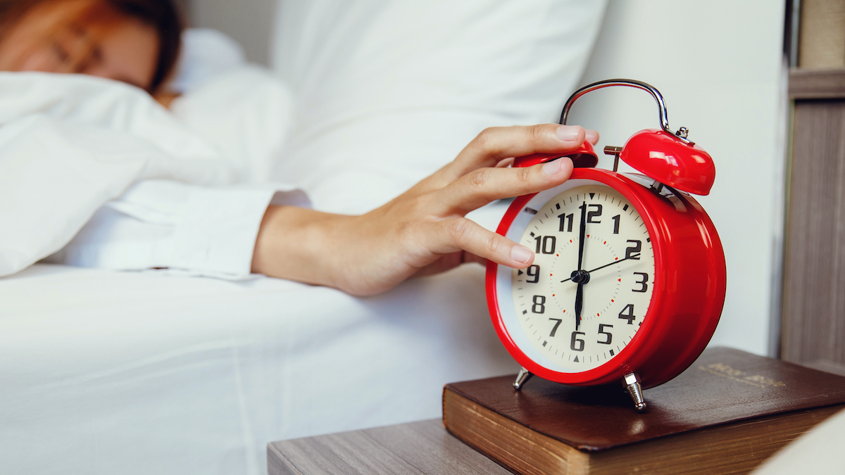 Woman in bed reaches across to her red alarm clock