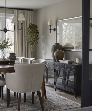 A dining room color idea with grey walls, dark wooden table, black sideboard and taupe curtains