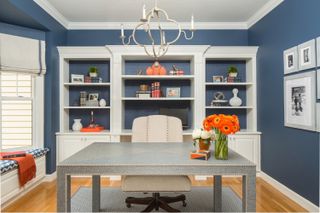 Home office with console desk and office chair, open shelving and cabinetry and window seat with blue walls and wood floor