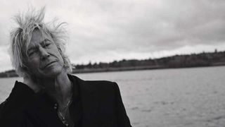 Duff McKagan standing by a river looking windswept