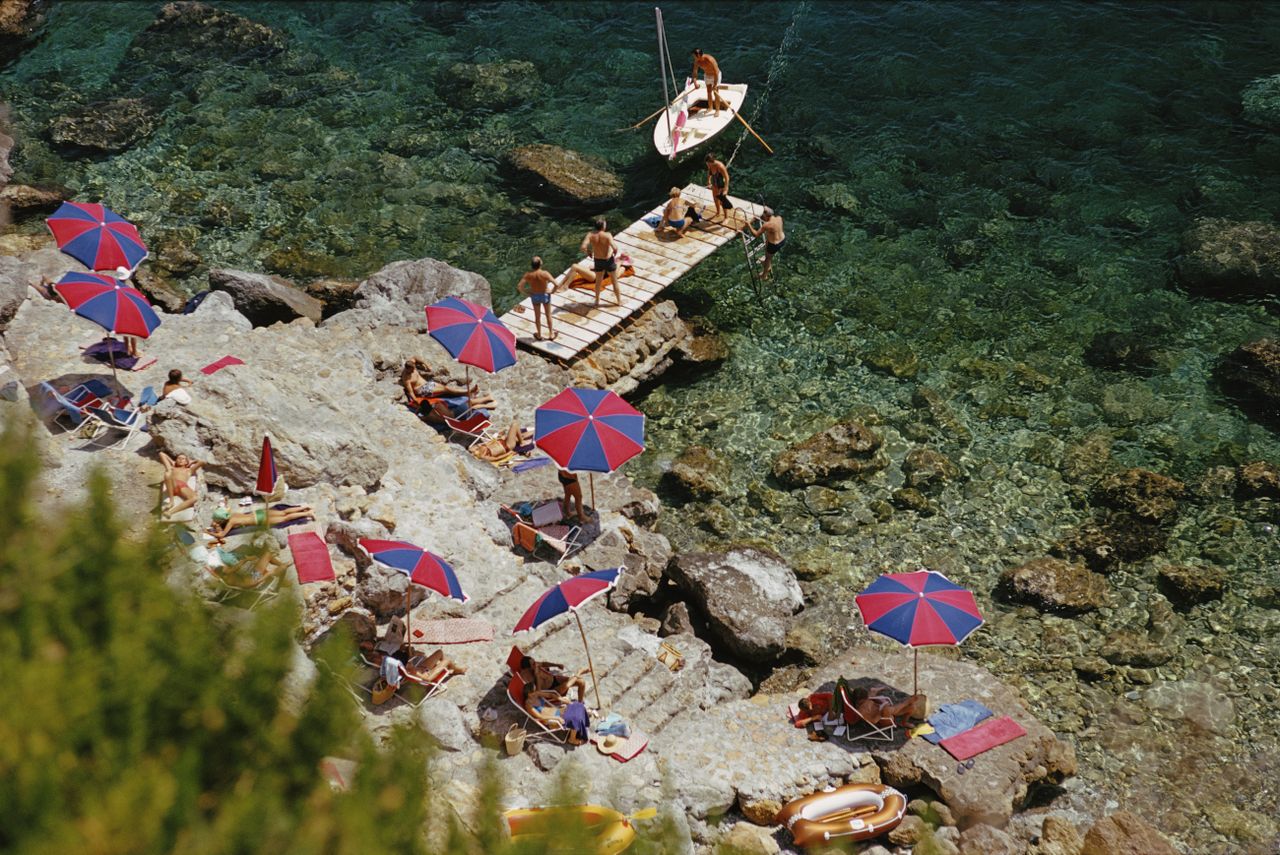 Birds eye view picture of people sunbathing under bright umbrellas, next to the beach