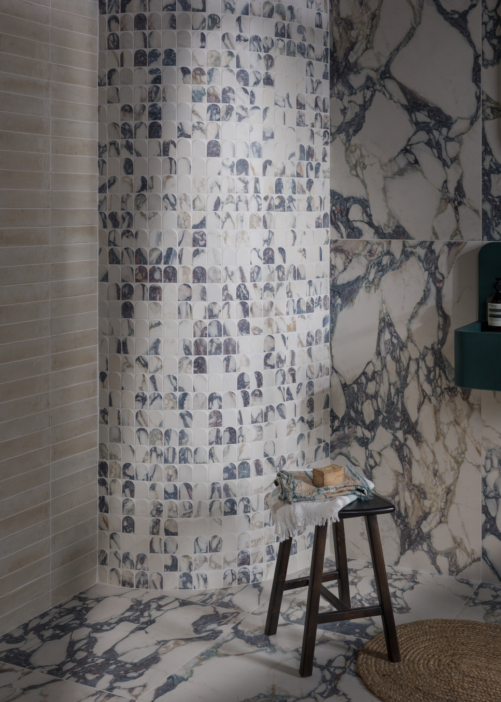 a marble tiled bathroom with a curved wall in small tiles, and large format marble tiles across the rest of the room