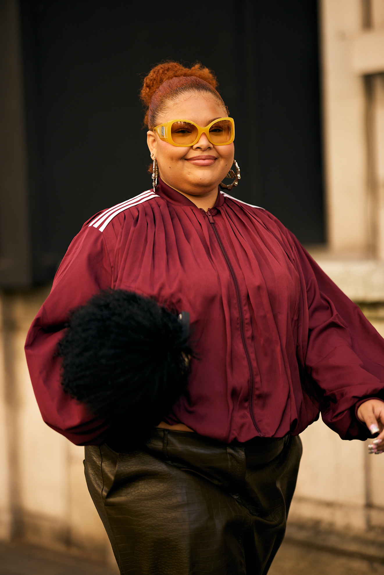 a white with red hair in a red jacket with a furry brown bag
