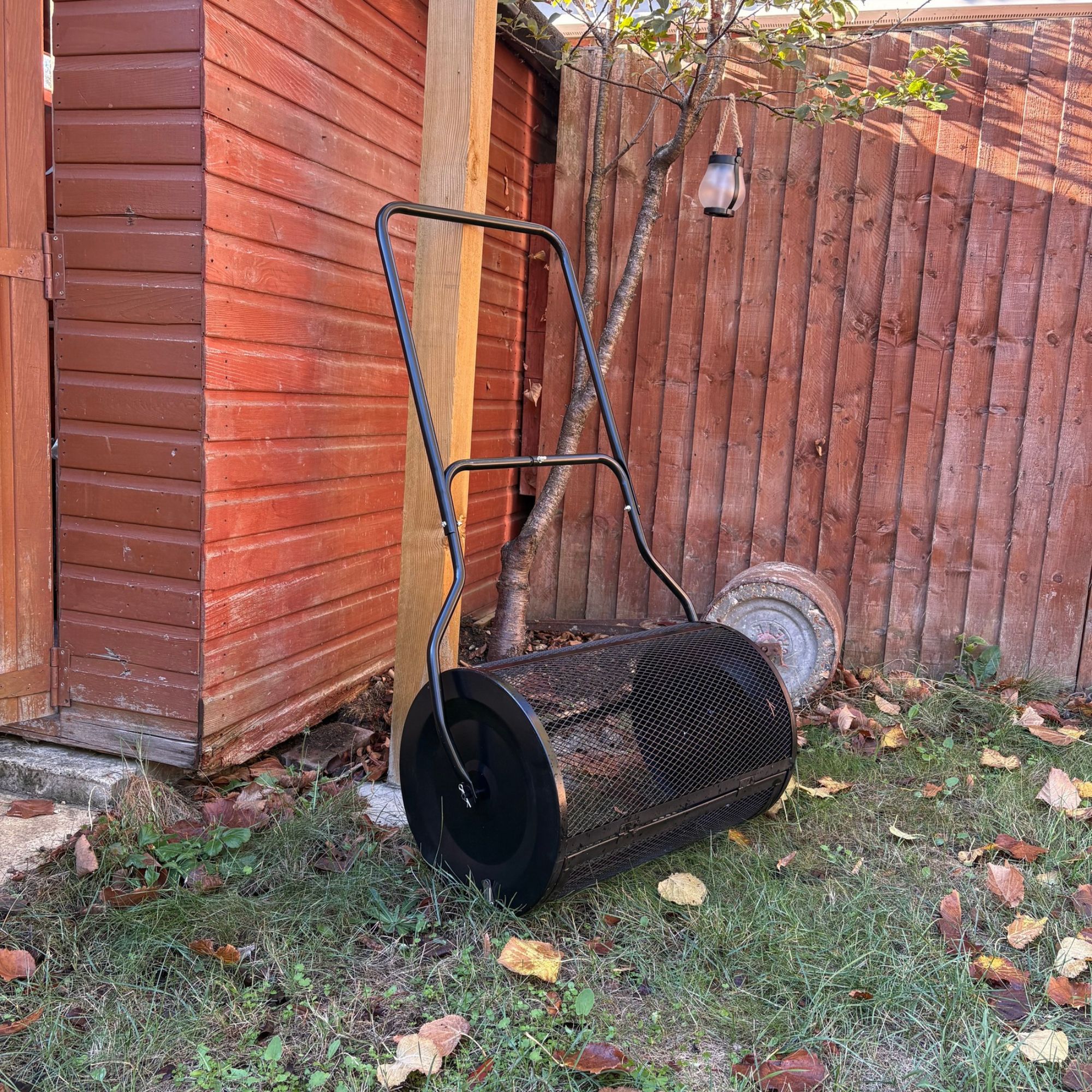 Outsunny Compost Spreader leaning against wooden post next to shed
