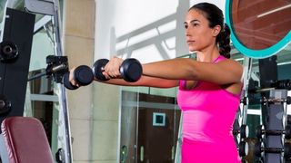 Woman performs front raise shoulder exercise with dumbbells