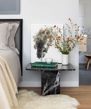 Detail of a bedroom with black marble bedside table and sheepskin rug
