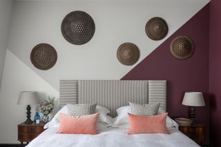 bedroom with grey and maroon walls, peach cushions, stripe headboard, side table, woven discs on wall