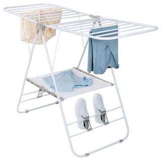 A gullwing white drying rack with clothes and shoes on it