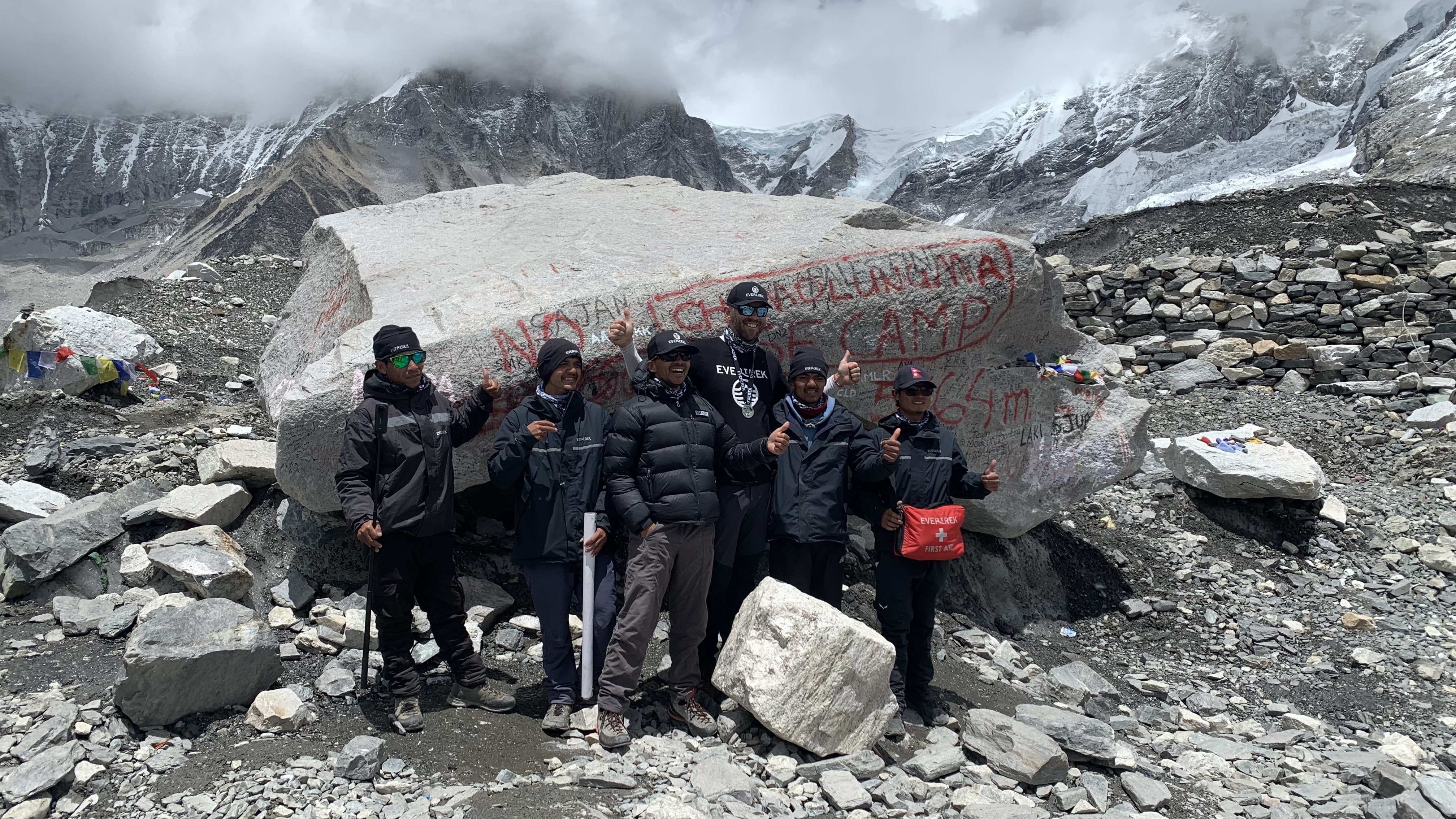Nepalese guides and porters in front of a large boulder with the words 'Chomolungma Base Camp' spray painted in red