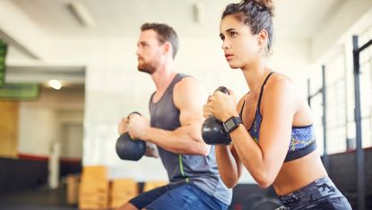 Man and woman both training with kettlebell weights
