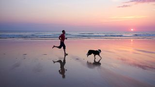 a man running on a beach with his dog