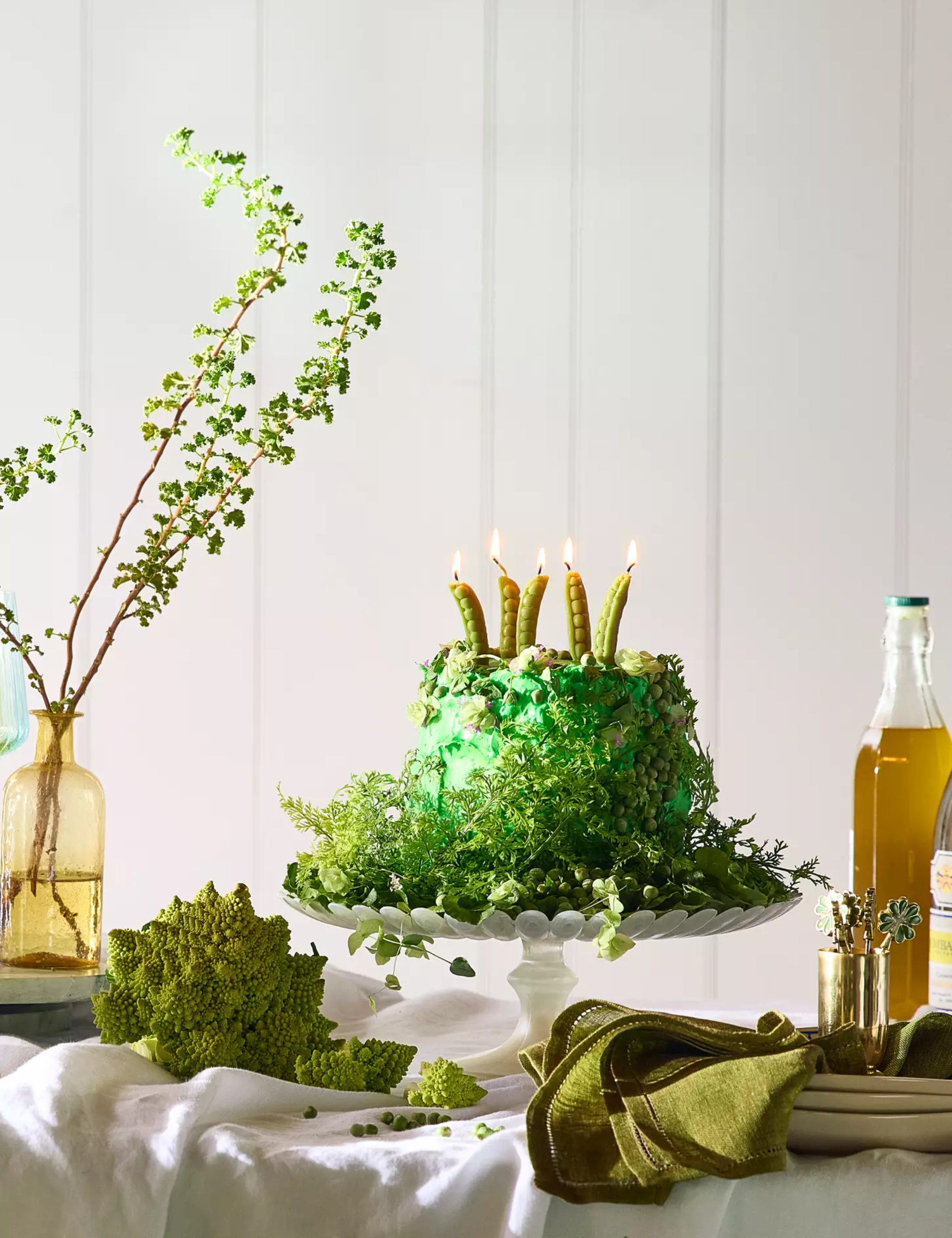 St. Patrick's Day tablescape featuring a green cake covered in moss alongside green table linens and shamrock-motif cocktail picks