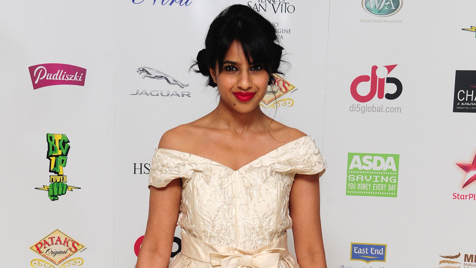 Ravinder Bhogal in a white dress poses in front of a sponsorship board