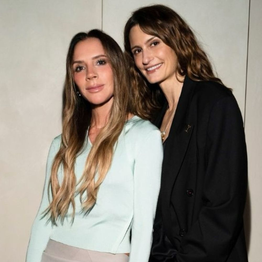 Victoria Beckham poses for a photo wearing a blush pink skirt with a turquoise top and pink satin shoes. 