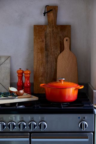 An orange Le Creuset Dutch casserole dish and salt and pepper mills on a stovetop