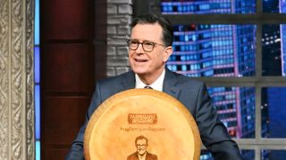 Stephen Colbert in front of giant cheese wheel with his face on it on The Late Show
