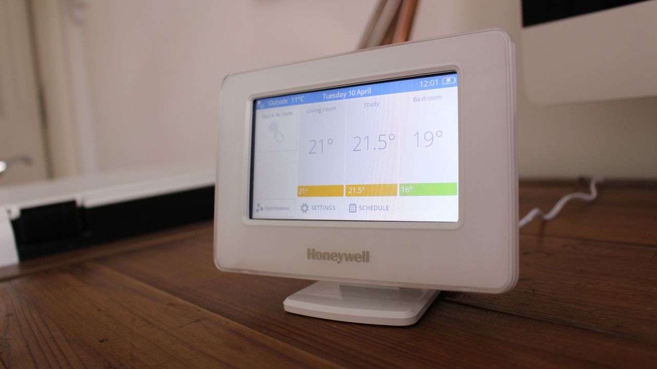 Honeywell Evohome smart thermostat main control unit on table, showing current ambient and target temperatures in living room, study, and bedroom