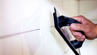 Person applying grout to white tile with a grout float