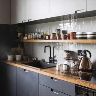 kitchen with white wall tiles, a wooden countertop and wooden shelf, dark grey cabinets and a silver kettle