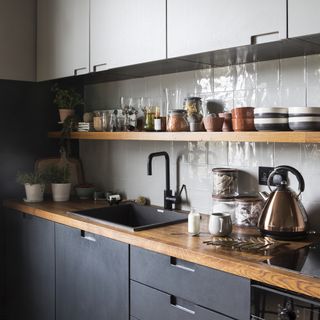 Kitchen with white wall tiles, wooden countertops and wooden shelves, dark gray cabinets, and a silver kettle