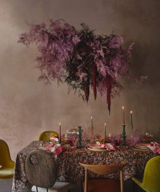 Trend-forward table settings for a dining table at Christmas, a tablecloth of various colors, and ice cream color palette of accessories, ornaments, plates and candles and feathery flower arrangement.