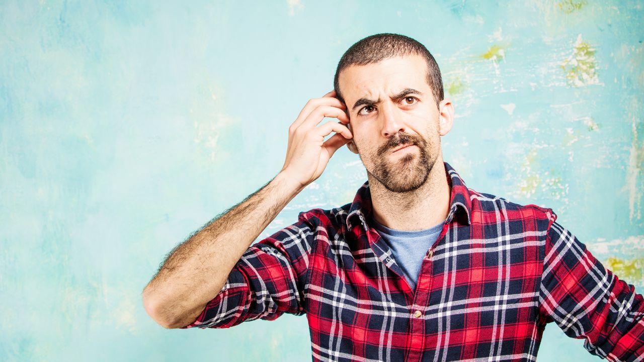 A man scratches his head with a questioning look on his face.