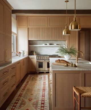 Wood kitchen with marble worktops, brass pendant lamps over an island and a floor runner