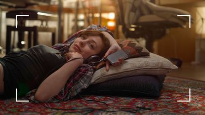 Woman lying on the floor holding phone above her head with headphones on, browsing audio erotica
