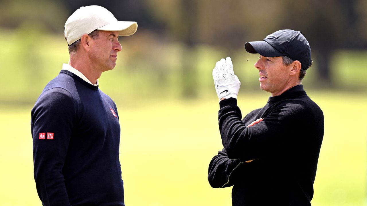 Rory McIlroy swats away a fly as he talks to Adam Scott during practice for the Australia Open