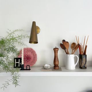 Floating shelf in a kitchen with gold wall light and wooden spoons stored in a white jug