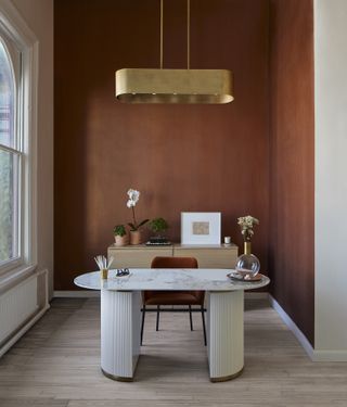 A home office in burgundy walls and gold lighting piece