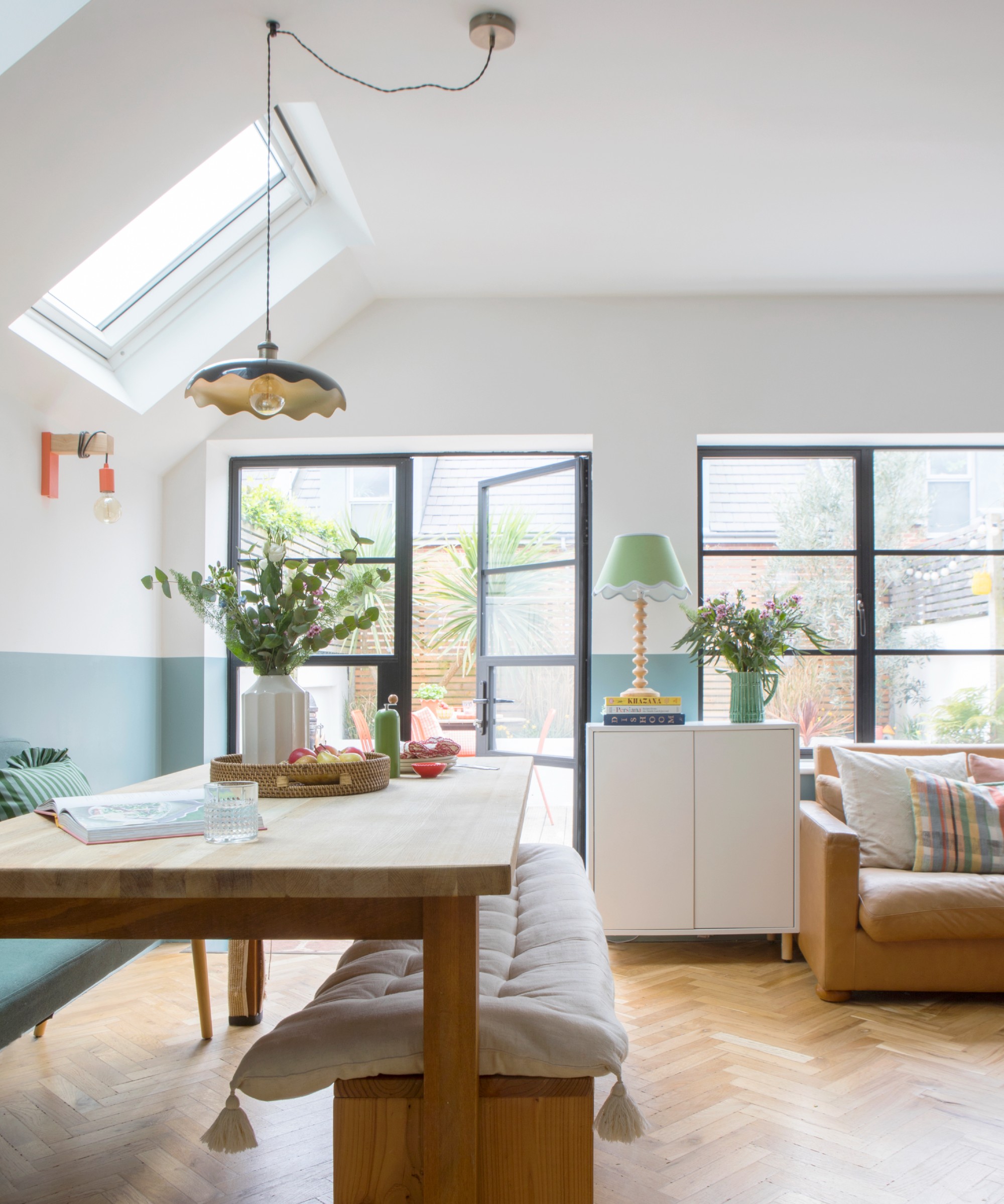 A dining area with a rectangular dining table and a bench with a scalloped pendant light hanging above