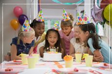 Children at a birthday party, crowded round a table ready to blow out candles on a birthday cake