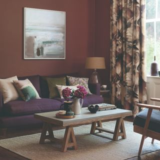 A brown-painted living room with botanical curtains and a purple sofa with a wooden coffee table