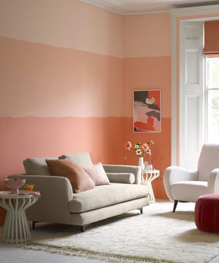 painted living room with striped feature wall in peach and orange shades, cream and white sofa and lounge chair, pink accessories