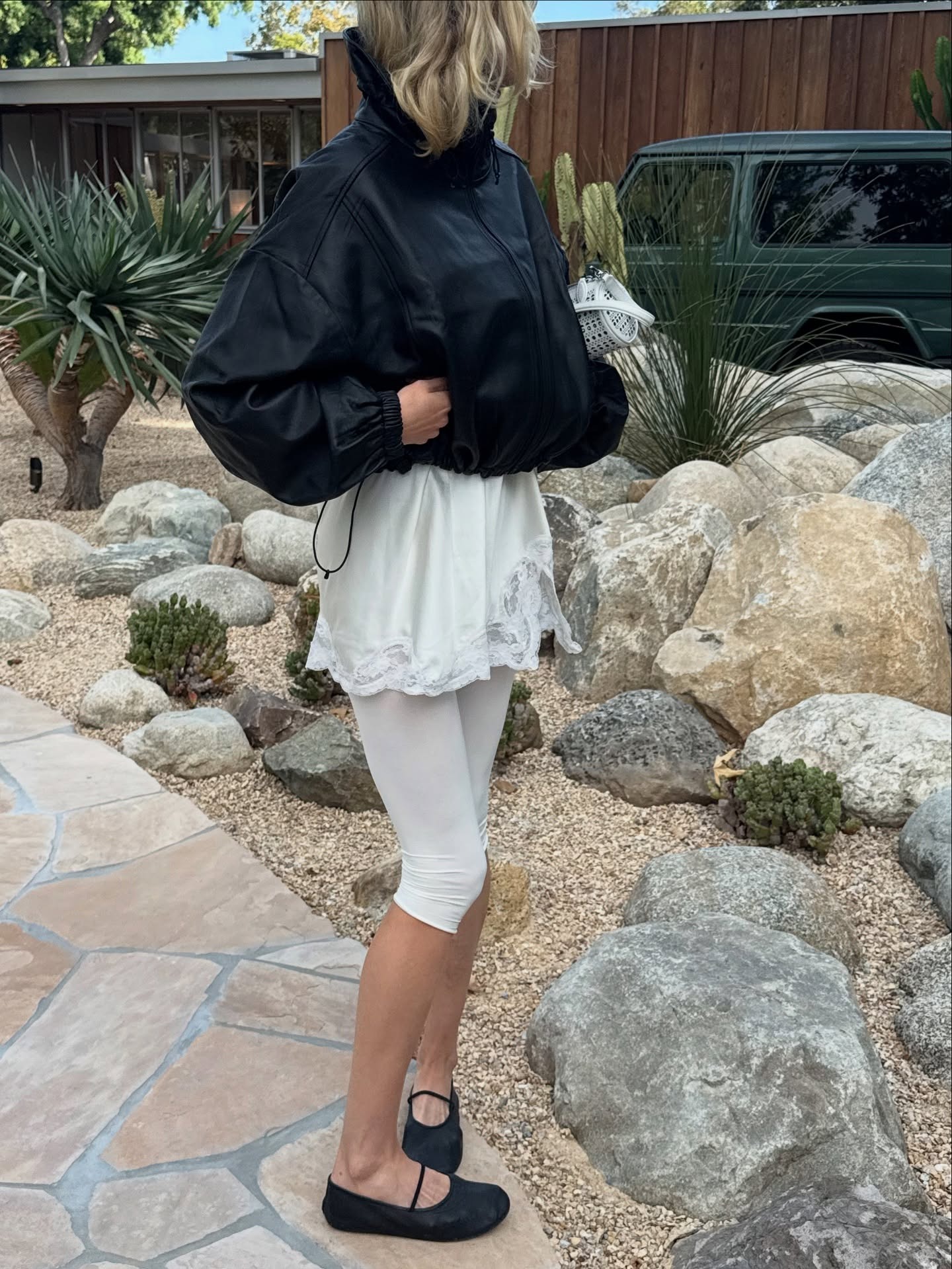 Elsa Hosk wearing a black windbreaker, a white lace slip, white capri leggings, and black Mary Jane flats