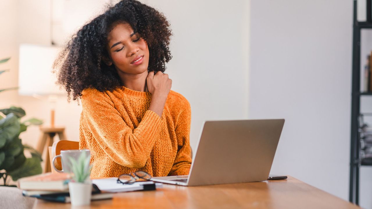 woman works at desk and hold shoulder in pain