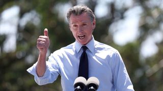 Governor of California Gavin Newsom, giving a thumbs up during a speech with out of focus trees behind him