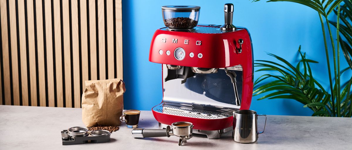 a red smeg espresso machine with burr grinder is photographed against a blue background