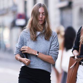 a woman wears a gray sweater with a Cartier tank watch and a black pencil skirt