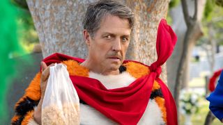 Hugh Grant holding a bag of cereal while dressed in the Tony the Tiger costume in Unfrosted.