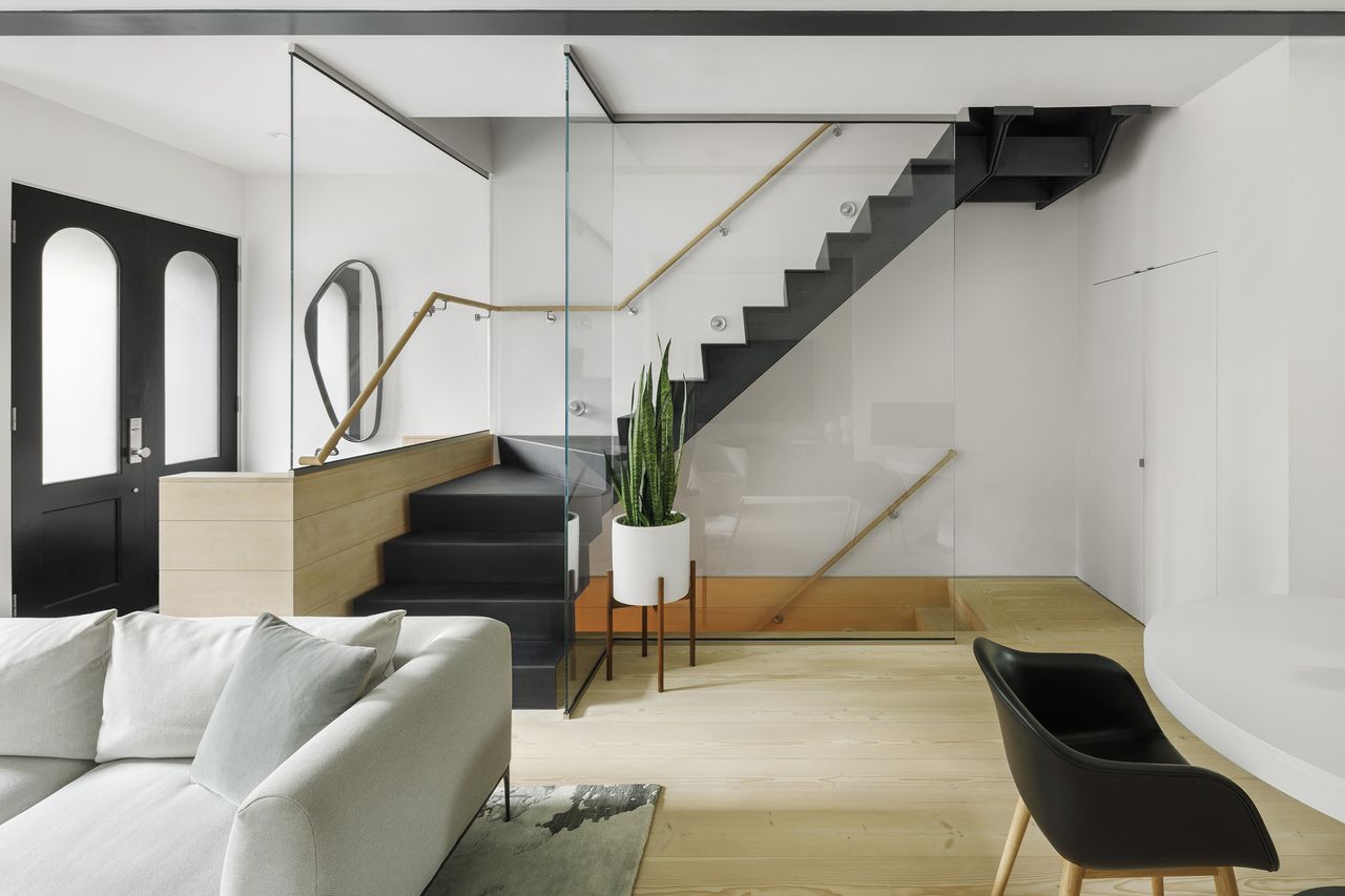 Interior with white couch, black chair and staircase and green plant in pot at the OverUnder House in Boston