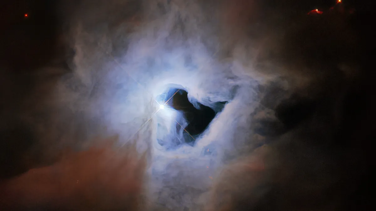 This peculiar portrait from the NASA/ESA Hubble Space Telescope showcases NGC 1999, a reflection nebula in the constellation Orion. It appears as a light blue cloud in space with a keyhole-shaped 'hole' in the center. (Image credit: ESA/Hubble & NASA, ESO, K. Noll)