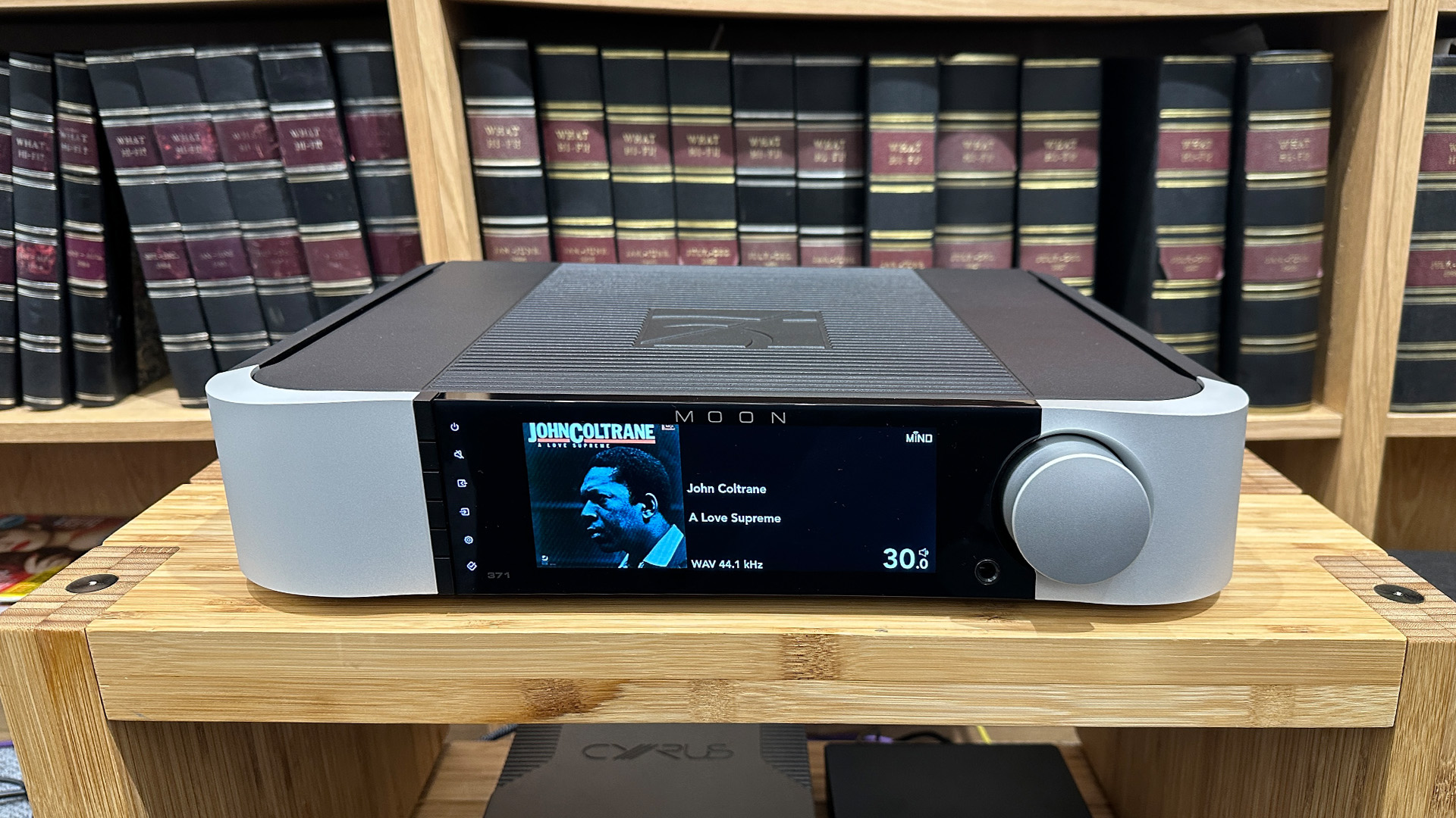 Moon 371 streaming amplifier on wooden hi-fi rack in front of bookcase