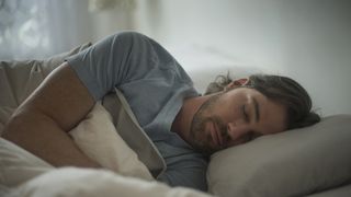 Cuántas horas de sueño necesitas: un hombre con camiseta azul durmiendo de lado