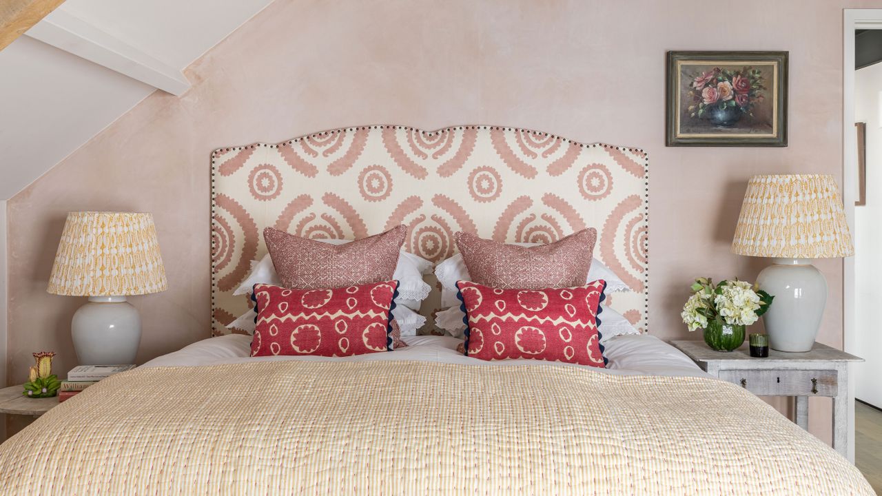 An example of bed ideas showing a bed with a pink and white upholstered headboard in front of a pink wall