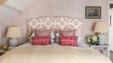 An example of bed ideas showing a bed with a pink and white upholstered headboard in front of a pink wall